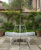 White garden bench and table set in a patio area with potted plants and a stone wall.