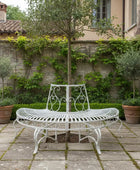 White metal garden bench in a stone-walled courtyard with greenery