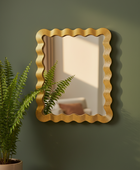 Gold-framed mirror on a green wall with a plant to the left.