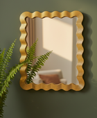 Decorative gold-framed mirror on a green wall with a plant in the foreground.