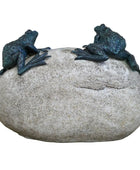 Two frog sculptures on a large stone with a blurred natural background