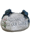 Decorative stone with 'Welcome to our Garden' text and frog sculptures on a wooden surface.