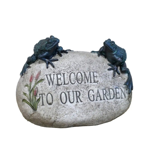 Decorative stone with 'Welcome to our Garden' text and frog sculptures on a wooden surface.