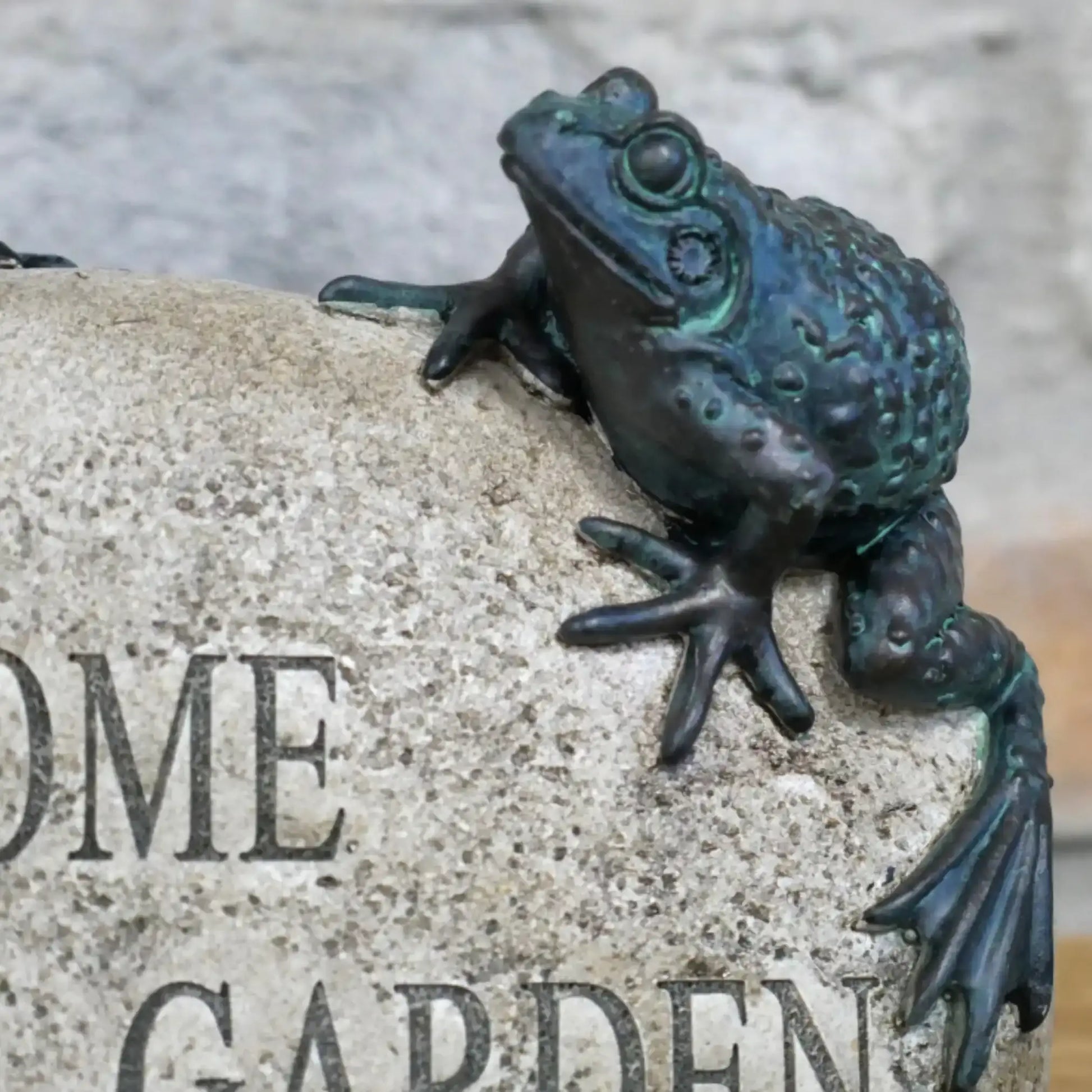Bronze frog sculpture on a stone with 'Welcome to our garden' engraved.