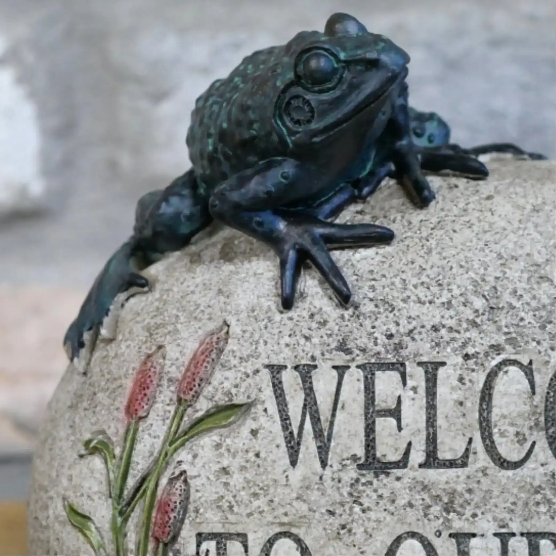 Bronze frog sculpture on a stone with 'Welcome' engraving