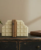 Decorative bookends shaped like white chocolate bars on a wooden surface with books and a plant.