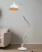 White floor lamp with a clear arm in a room with a beige sofa and a plant.