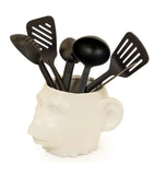 White head-shaped kitchen utensil holder with black utensils on a white background