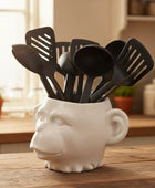 White ceramic container with black kitchen utensils on a wooden surface in a kitchen setting.