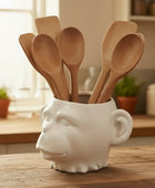 White ceramic container with a face design holding wooden spoons on a kitchen counter.