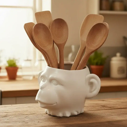 White ceramic container with a face design holding wooden spoons on a kitchen counter.