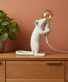 Decorative rat sculpture holding a light bulb on a wooden surface.