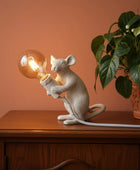 White mouse-shaped lamp holding a light bulb next to a vase of flowers on a neutral background