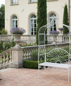 Decorative white metal bench in a garden setting with a mansion in the background