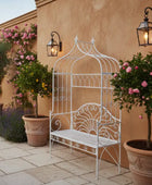 Decorative white metal bench with floral and potted plants in an outdoor setting.