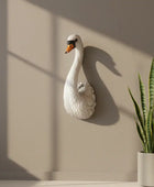Decorative swan wall sculpture on a beige wall with a potted plant below.