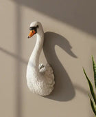 White swan wall sculpture on a beige wall with a plant to the right.
