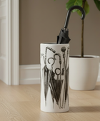 Decorative vase with black abstract design on a wooden floor in a room with a plant and furniture.