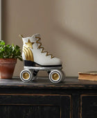White roller skate with gold accents on a wooden surface next to a plant and book.