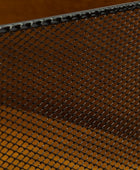 Close-up of a black metal mesh screen or grate with a diamond-pattern weave over a warm brown background.