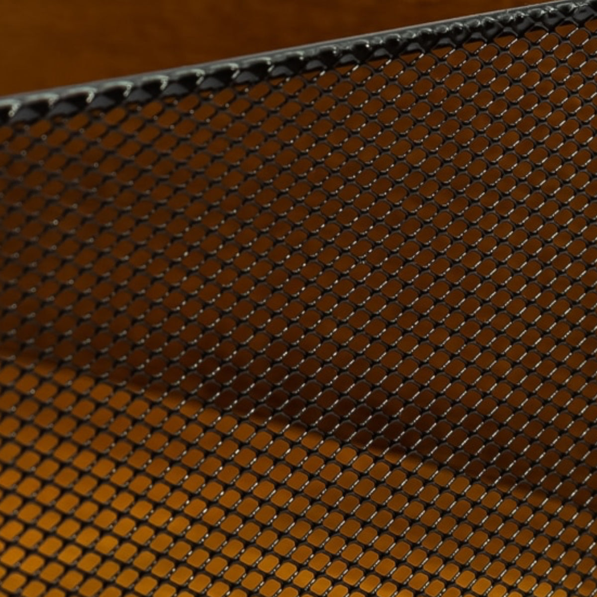 Close-up of a black metal mesh screen or grate with a diamond-pattern weave over a warm brown background.
