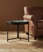 Brown leather armchair and round black table in a room with a plant and window.