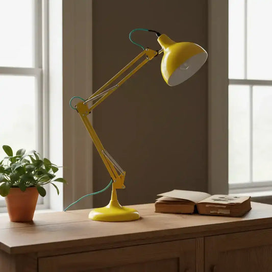 Yellow adjustable desk lamp on a wooden surface with a plant and book in the background