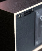 Close-up of the side and back corner of a rectangular wooden box or speaker-like device, showing a dark wood grain exterior, a black textured panel, screws, and a mounting area.