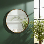 Round mirror with wooden frame on a green wall with a plant in the corner