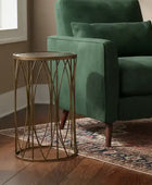 Gold side table next to a green armchair in a room with wooden flooring and a window.
