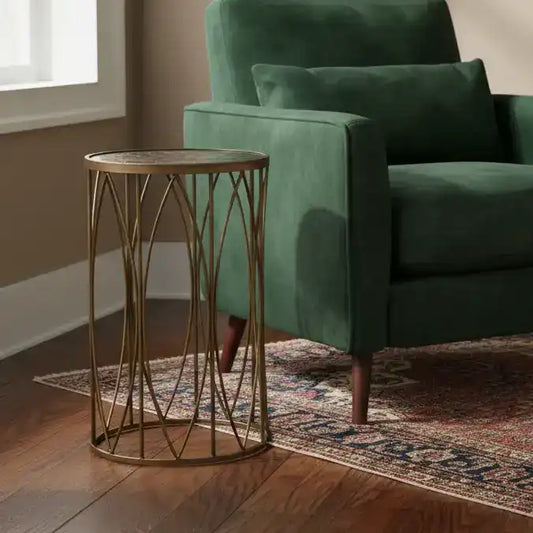 Gold side table next to a green armchair in a room with wooden flooring and a window.