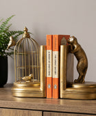 Gold-toned decorative bookends shaped like a birdcage with birds and a bear, holding two books against a dark background.