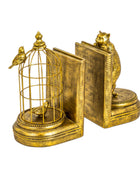 A pair of ornate gold-toned bookends shaped like books, with a birdcage and small birds on one end and a cat standing on the other, shown on a plain white background.