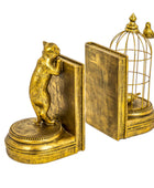 A pair of ornate gold-toned bookends shaped like old books, with one end featuring a small cat figurine and the other featuring a birdcage with birds, shown on a plain white background.