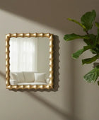 Gold-framed mirror on a wall with a plant to the right