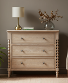 Wooden dresser with a lamp and plant in a room setting