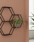 Hexagonal black wall shelf with a plant against a brown wall