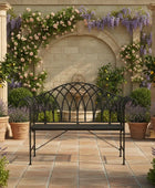 Decorative outdoor setting with a black metal bench, stone archway, and potted plants.