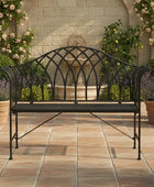 Wrought iron bench on a patio with a fountain and flowers in the background
