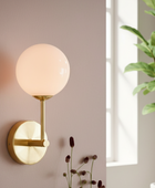 Modern wall sconce with a spherical glass shade in a room with a window and plant.