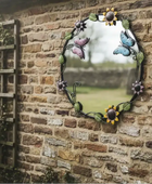 Decorative garden mirror with floral and butterfly design on a brick wall.