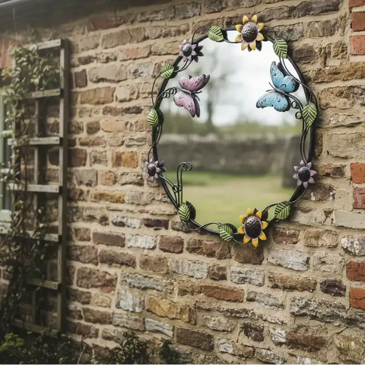 Decorative garden mirror with floral and butterfly design on a brick wall.