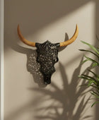 Decorative bull skull with wooden horns on a wall next to a plant