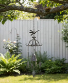 Decorative wind chime hanging from a tree branch in a garden setting.