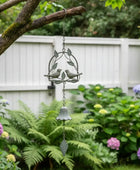 Decorative wind chime with birds and a bell hanging from a tree branch in a garden.