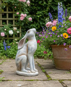 Statue of a rabbit in a garden with flowers and a wooden fence in the background
