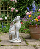 Statue of a rabbit sitting on a garden path with flowers in the background