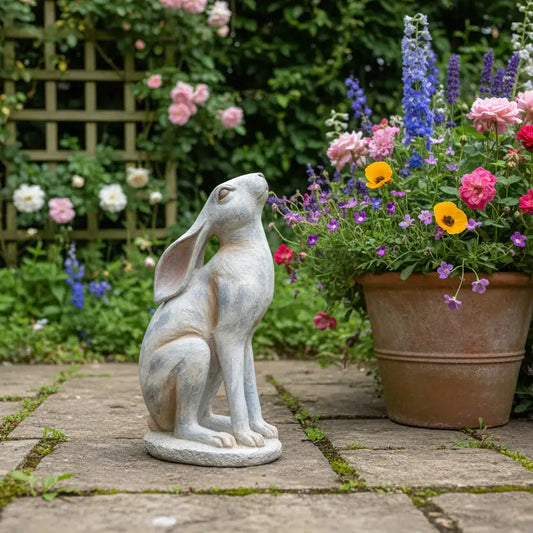 Statue of a rabbit sitting on a garden path with flowers in the background