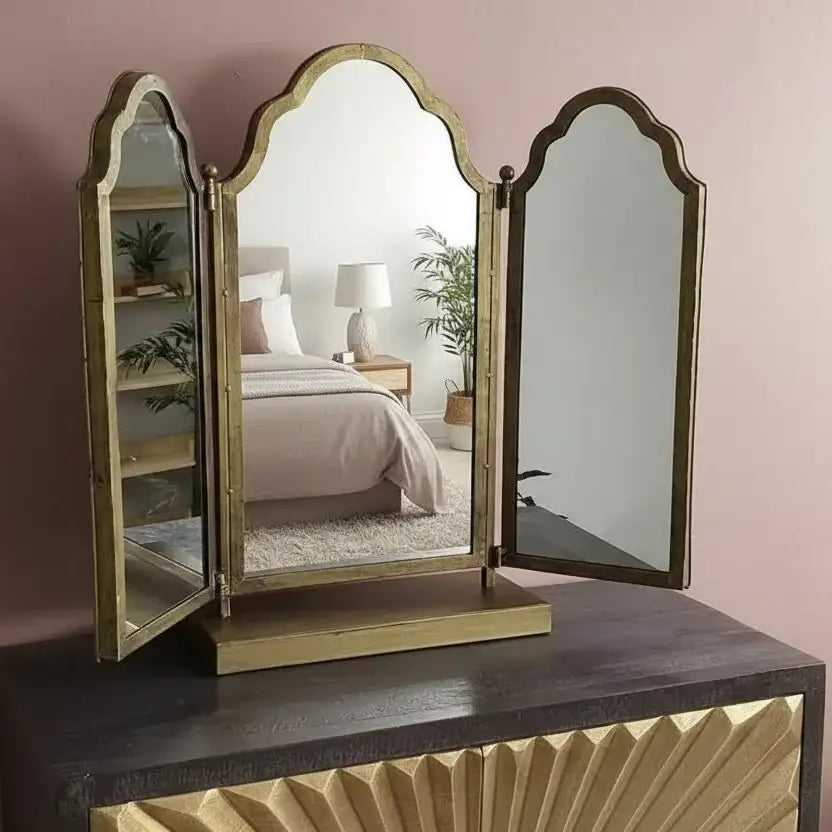 Tri-fold vanity mirror on a dresser with a bedroom in the reflection