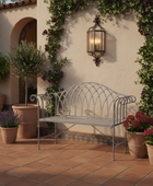 Decorative metal bench on a patio with potted plants and a wall sconce.